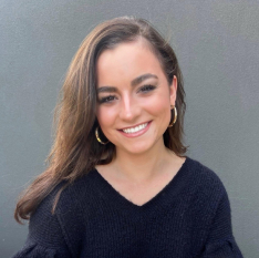 a woman wearing a black sweater and gold hoop earrings smiles for the camera